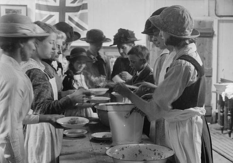 Women serving food to children around a long table