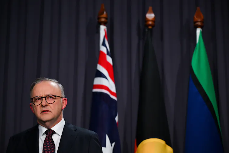 Anthony Albanese speaking in front of flags.