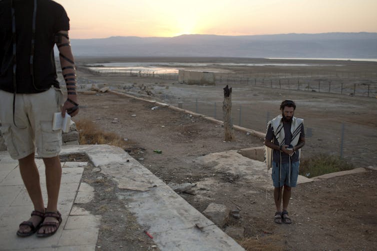 Two men seen at prayer on a terrace with the rising sun in the background.