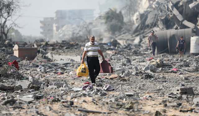 Man carrying bags walks through piles of rubble.