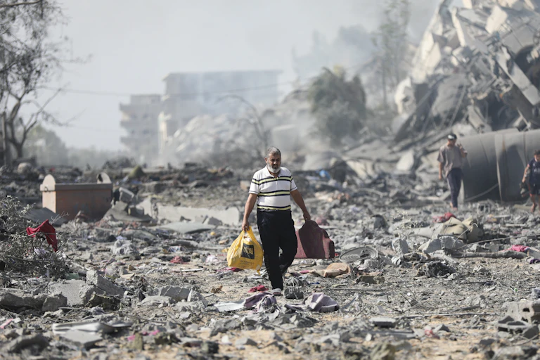 Man carrying bags walks through piles of rubble.