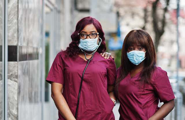 Two women in maroon scrubs wearing face masks