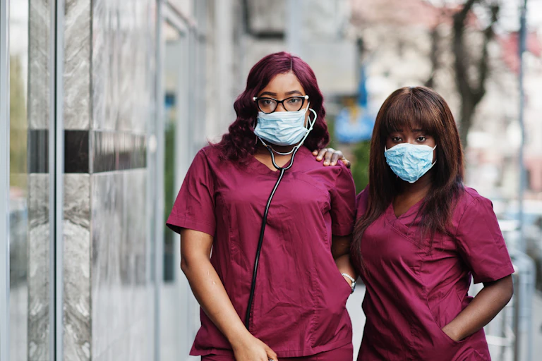Two women in maroon scrubs wearing face masks