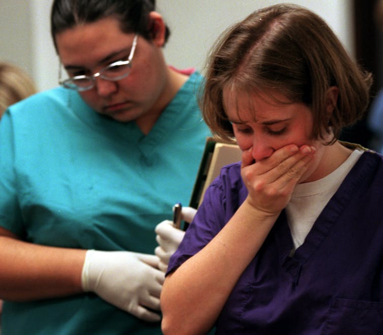 Two medical students, intently looking down, with one covering her mouth with one hand.