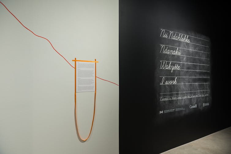 A red line seen traced along a wall surrounding a text description, next to a wall showing chalked handwriting along lines.