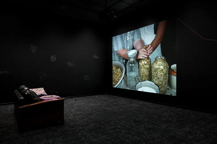 A chair facing a screen showing hands on a jar in a space with black walls and black floor.