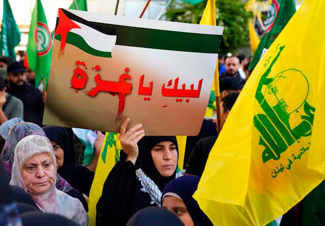 Hezbollah supporters in a rally hold flags and signs, including one that reads in Arabic: ‘We are with you Gaza.’