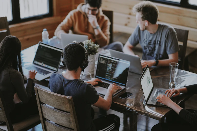 A group sits around a table with laptops.