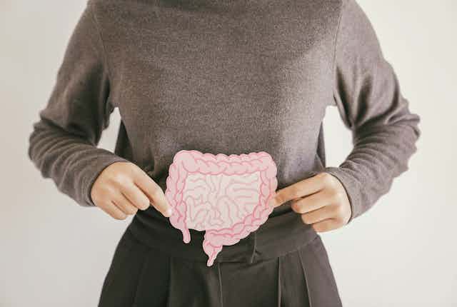 A woman holds a paper cutout of a gut over her stomach.