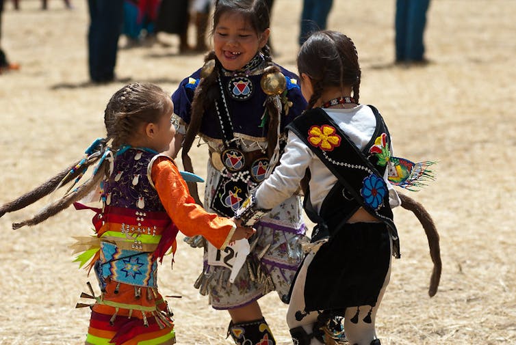 Three American Indian children in traditional dress dance in a circle