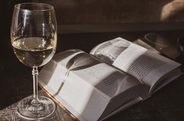 A glass of white wine sits next to a thick open book.