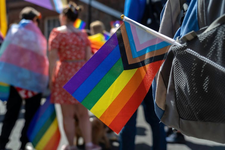 An LGBTQ+ flag hangs out of a bag