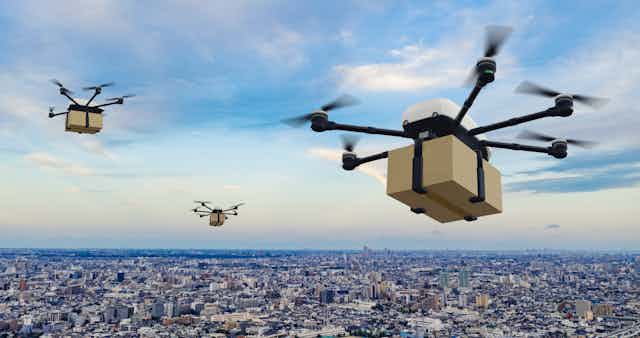 Drones carrying boxes over a city.