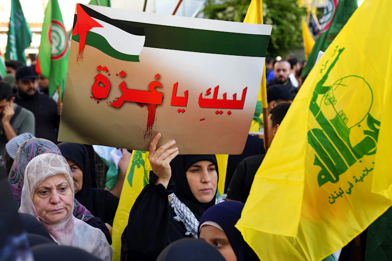 Hezbollah supporters in a rally hold flags and signs, including one that reads in Arabic: ‘We are with you Gaza.’