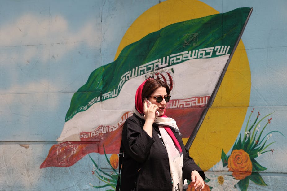 Une femme iranienne passe devant un drapeau iranien peint sur un mur dans une rue de Téhéran