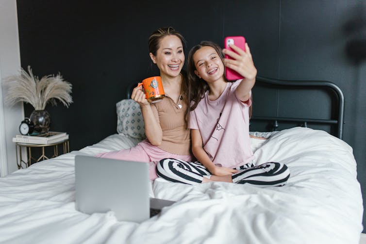 A mom and daughter with a laptop and cellphone having fun.