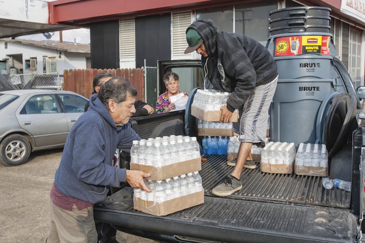 Des habitants d'East Porterville, en Californie, soulèvent des palettes d'eau en bouteille à l'arrière d'un camion.