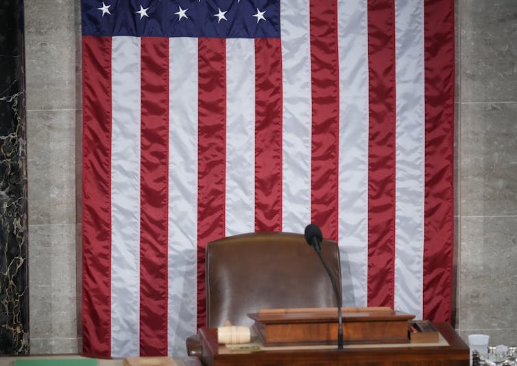 An empty leather chair behind a lectern and in front of an American flag.