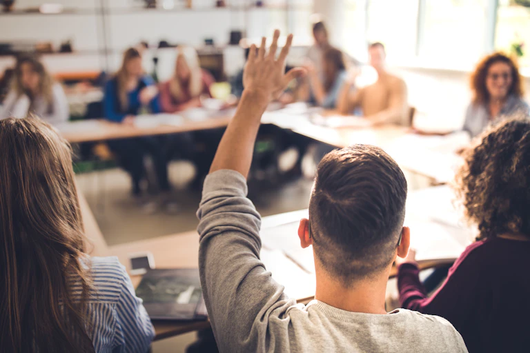 college class, man raising hand, facing away from camera