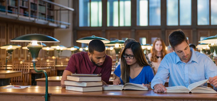 three students looking at textbooks in library