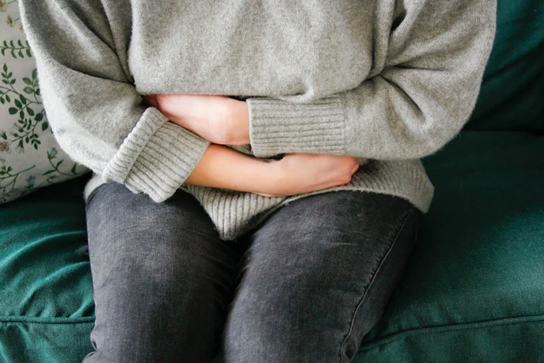 Person in gray sweater and black jeans hugging their torso in pain.