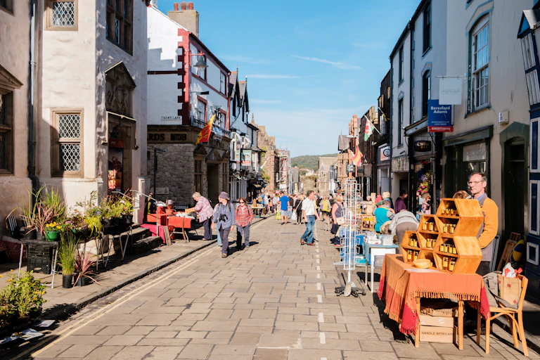 Man at stall selling honey on a high street with other outside vendors and people walking.