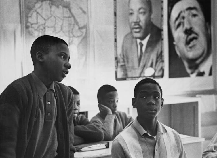 A classroom with Black students has large photographs of Black leaders and a map of Africa.
