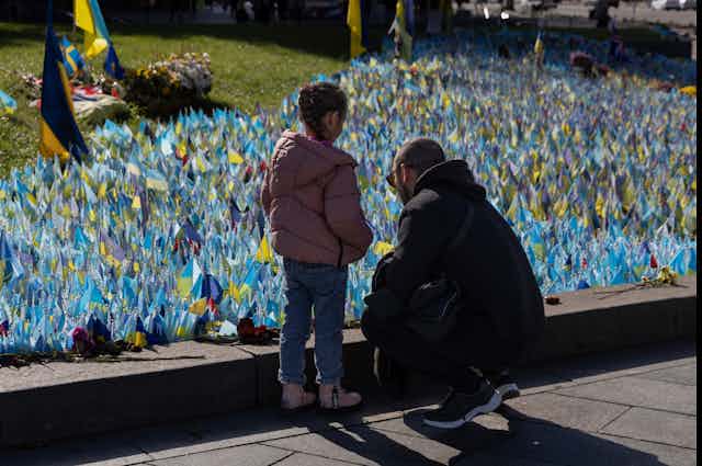 A man and young girl stand near a collection of blue and yellow flags.