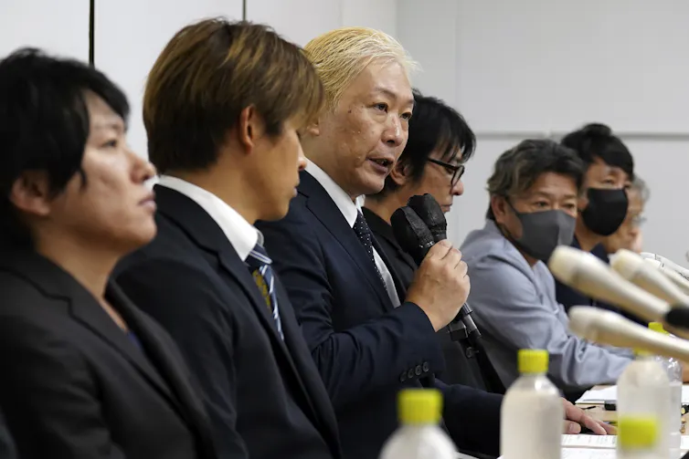 A line of seated men at a long table with sombre faces.