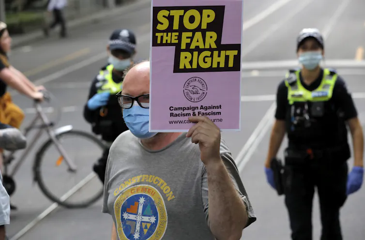 A man in a face mask holds a sign that reads 'stop the far right' in Melbourne.