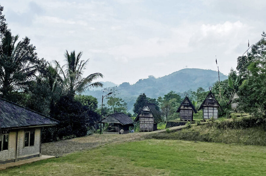 a verdant landscape on top of a high lookout with five simple houses with what appears to be thatched rooms