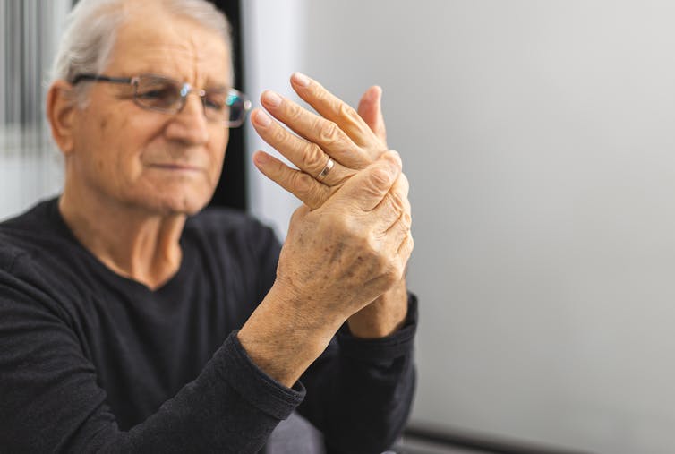 A senior man holds one hand in his other hand.