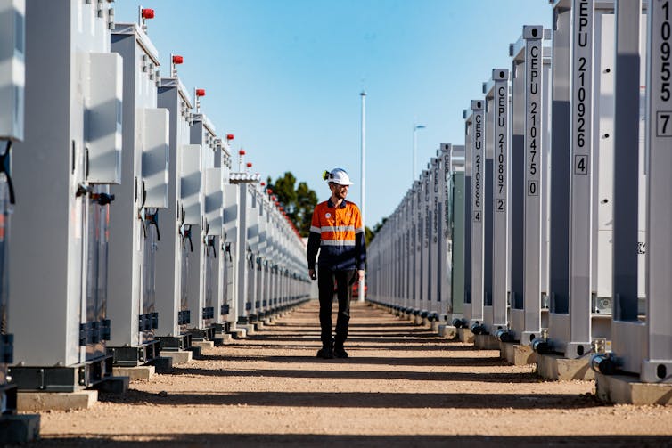 a worker walking between large batteries at a grid battery installation