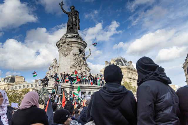 A photo of protesters with Palestinian flags in front of a statue.