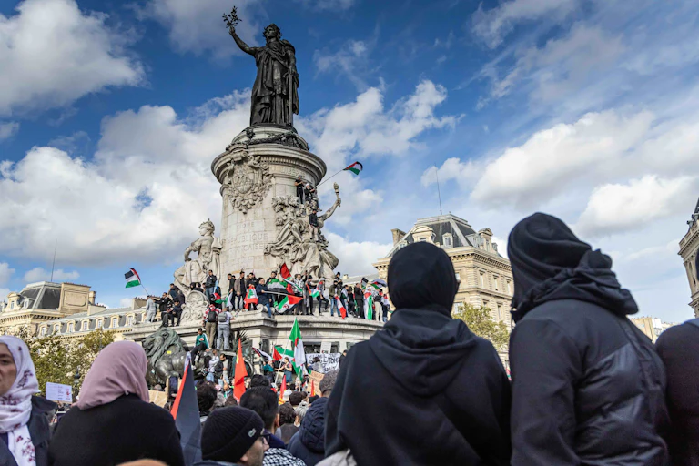 A photo of protesters with Palestinian flags in front of a statue.