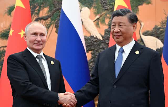 PUtin and Xi shaking hands in front of their national flags.