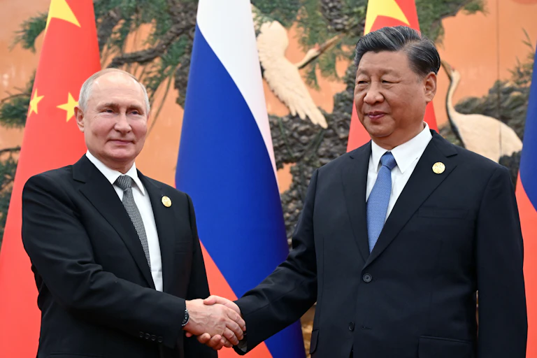 PUtin and Xi shaking hands in front of their national flags.