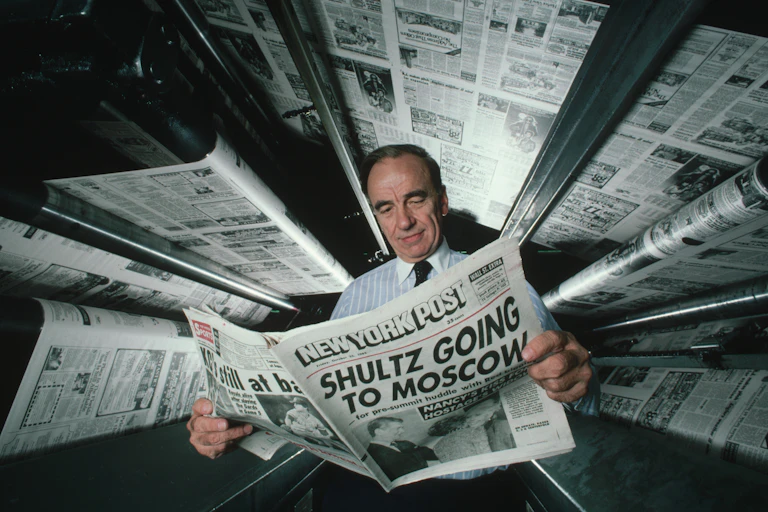 A man in shirt and tie reads a newspaper as printing presses show pages above his head.