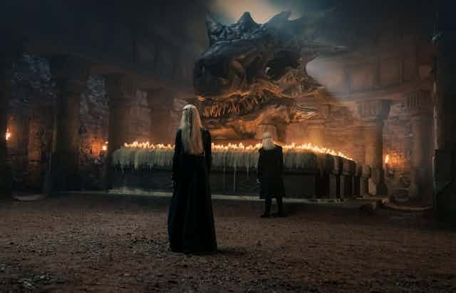 Un hombre y una mujer, de espaldas, observan el inmenso cráneo de un dragón.