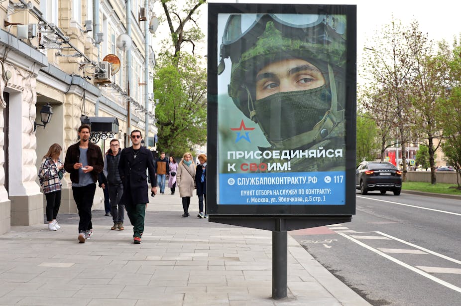Des passants dans une rue de Moscou, devant une affiche de recrutement de l'armée russe