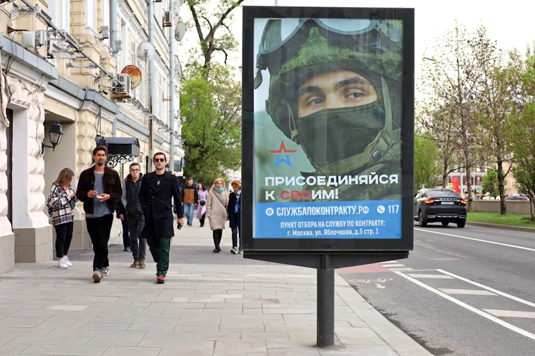 Des passants dans une rue de Moscou, devant une affiche de recrutement de l'armée russe