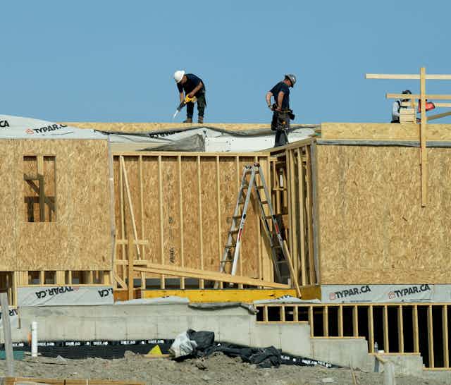 Two workers stand atop a house under construction.