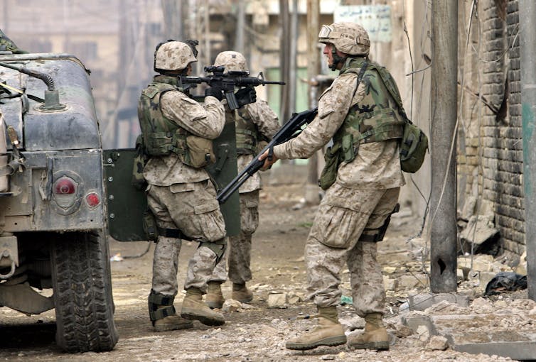 Soldiers in camouflage move through a cityscape.