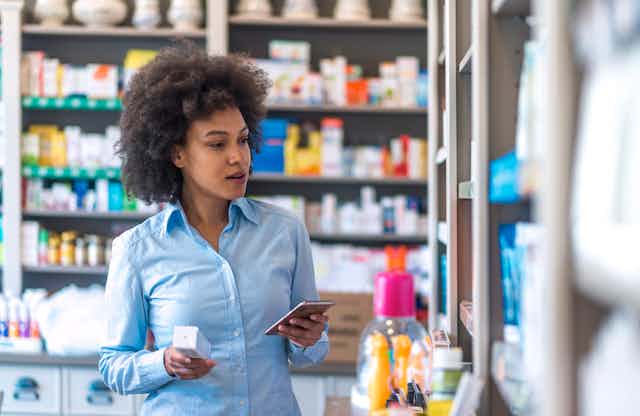 Young woman choosing medicine standing with phone in a pharmacy.
