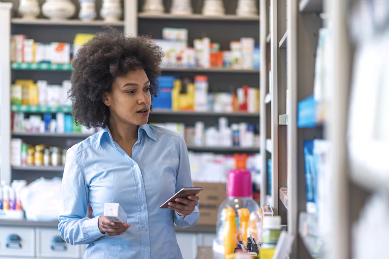 Young woman choosing medicine standing with phone in a pharmacy.