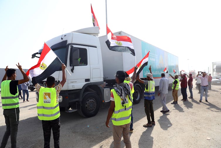 Des personnes portant des gilets jaunes brandissent des drapeaux égyptiens devant un grand camion blanc.