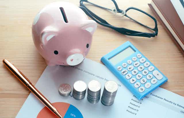 A piggy bank, a calculator, a pen and several stacks of coins sitting on a desk