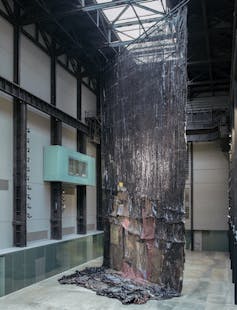 A large black sculptural form hangs from the roof, gathering on the floor.