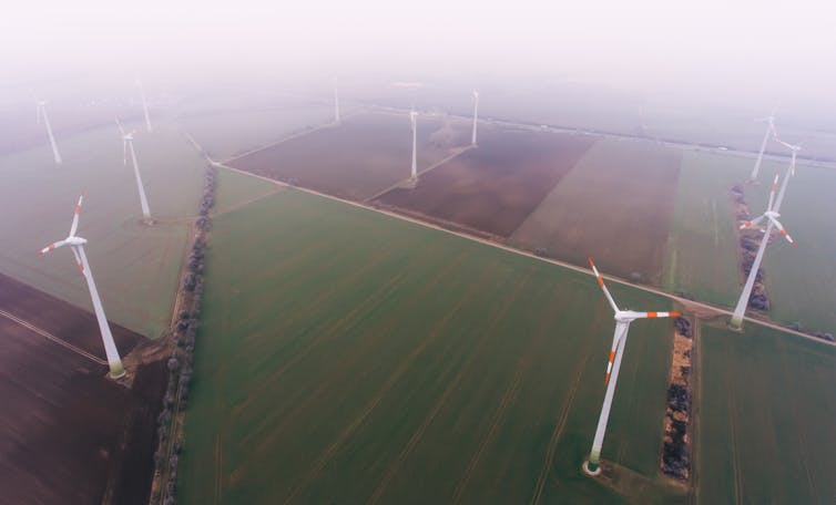 Aerial shot of static wind turbines in a foggy field.