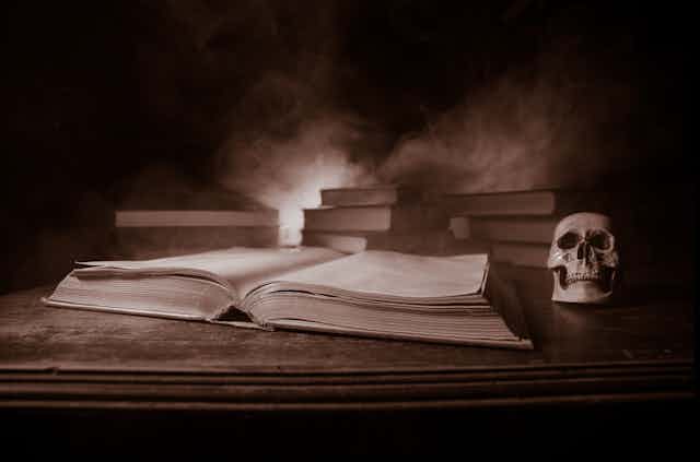 A sepia photograph of an open book with a skull next to it. 